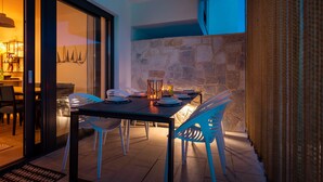 An outdoor dining area with a stone wall, a table set for four, and blue chairs. - Villa Navy Lemon (Vodice)