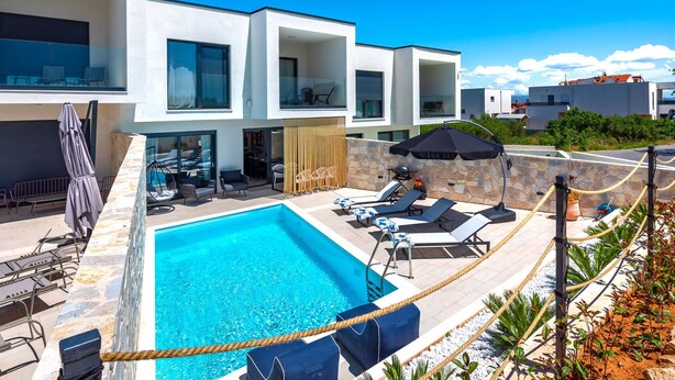 A modern residential building with a swimming pool, outdoor seating, and a stone wall. - Villa Navy Lemon (Vodice)