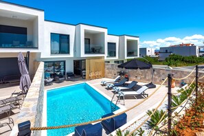 A modern residential building with a swimming pool, outdoor seating, and a stone wall. - Villa Navy Lemon (Vodice)