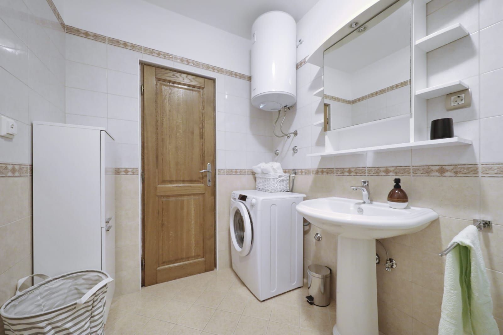 A bathroom with a washing machine, a sink, a mirror, and a towel rack.