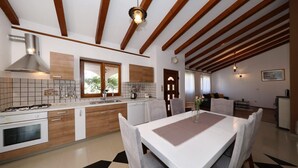 Una cocina moderna con vigas de madera, un comedor con mesa para cuatro y un salón con sofá y televisor.