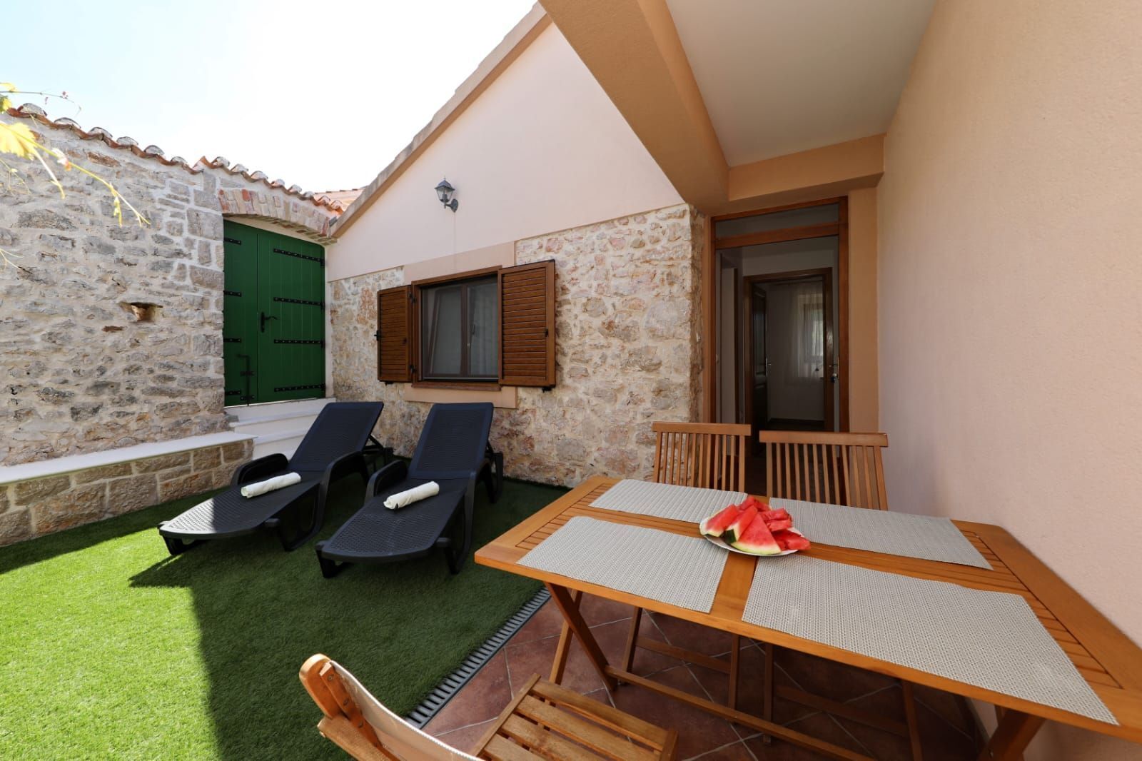 Un pequeño patio al aire libre con dos sillones, una mesa con camino de mesa y una puerta verde.