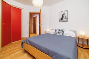 Une chambre avec un lit, une armoire rouge, une porte donnant sur une autre pièce, un tableau représentant la Tour Eiffel accroché au mur et des lampes de chevet.