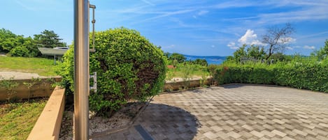 A paved outdoor area with a metal structure, a hedge, and a view of the sea.