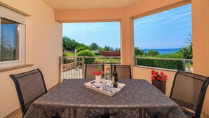 A balcony with a table set for two, featuring a bottle, glasses, and a tray with flowers. - Apartment Ereiz (Crikvenica)