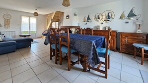 Ein geräumiger Wohnbereich mit einem Esstisch für vier Personen, umgeben von Holzstühlen. Ein blaues Sofa steht an der Wand, und eine Treppe führt auf eine obere Ebene.