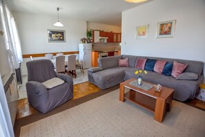 A living room with a grey sofa, a matching armchair, and a wooden coffee table. There is a dining area with a white table and chairs, and a kitchen in the background. - Apartments Jasmine (Biograd na Moru)