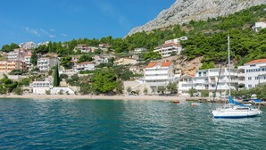 A coastal town with buildings on a hillside, a beach, and a sailboat in the water. - Apartments Olive sea View (Omis)