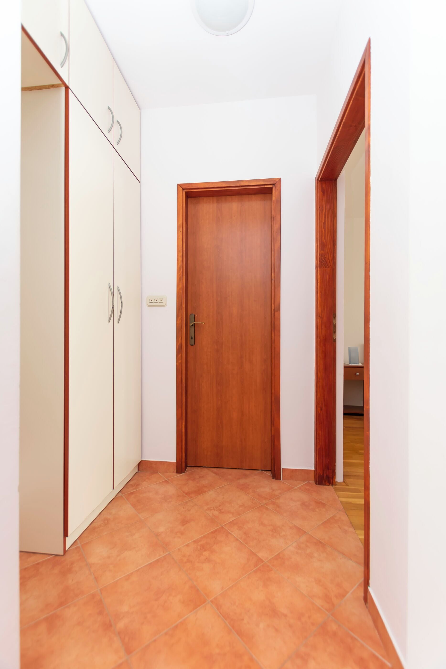 A hallway with a wooden door, white wardrobe, and tiled floor.