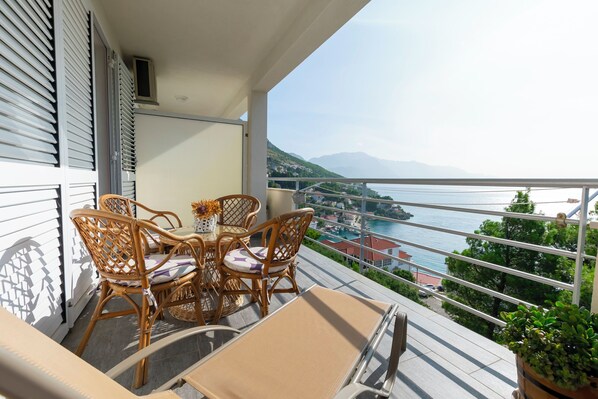 Een balkon met rieten meubilair, uitzicht op een meer en een bergketen in de verte.