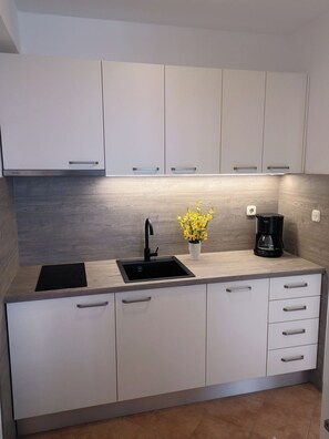 A modern kitchen with white cabinets, a black sink, a coffee maker, and a small potted plant. - Apartments Olive sea View (Omis)