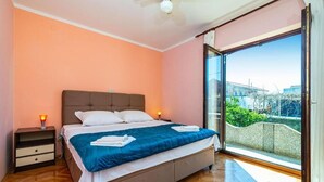 A bedroom with a bed, nightstands, a ceiling fan, and a large sliding glass door leading to a balcony. - Apartment Serda (Preko)