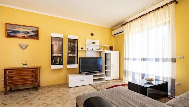 A room with a TV, white shelving, a wooden dresser, and a bed. - Apartment Serda (Preko)