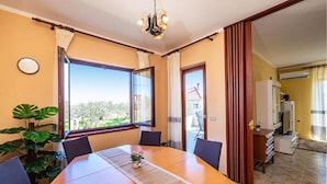 A dining area with a wooden table, chairs, a potted plant, and a view through the window. - Apartment Serda (Preko)