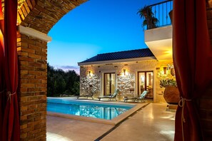 A poolside view of a stone building with a balcony, lounge chairs, and a swimming pool. - Villa Pamaroka (Sibenik)