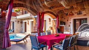 An outdoor dining area with a red tablecloth, surrounded by chairs, under a netted ceiling. - Villa Pamaroka (Sibenik)