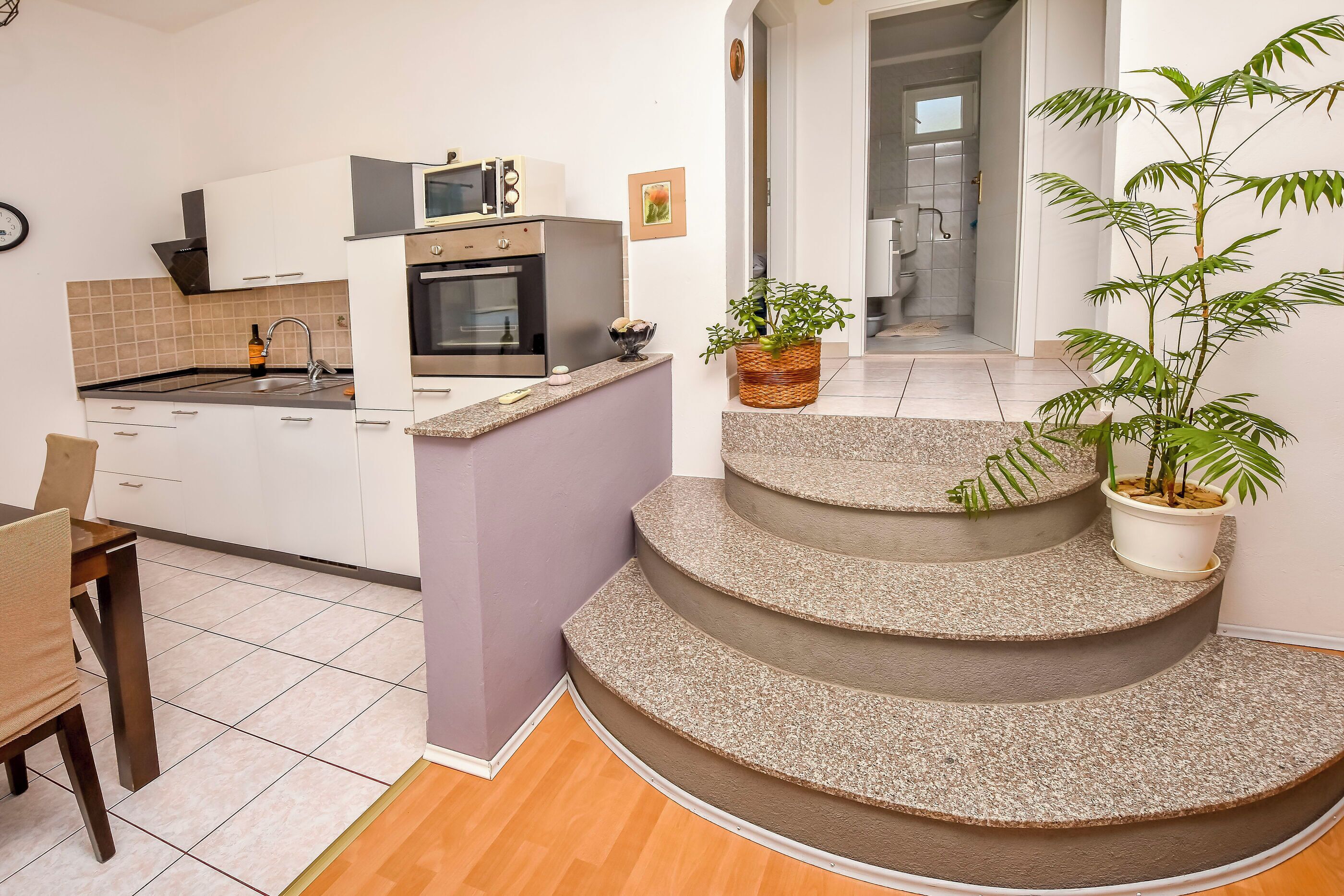 Una cucina moderna con mobili bianchi, un forno a microonde e un lavello. Ci sono due piante in vaso su una scalinata.