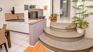 A modern kitchen with white cabinets, a microwave, and a sink. There are two potted plants on a staircase. - Apartment Burin (Pakostane)