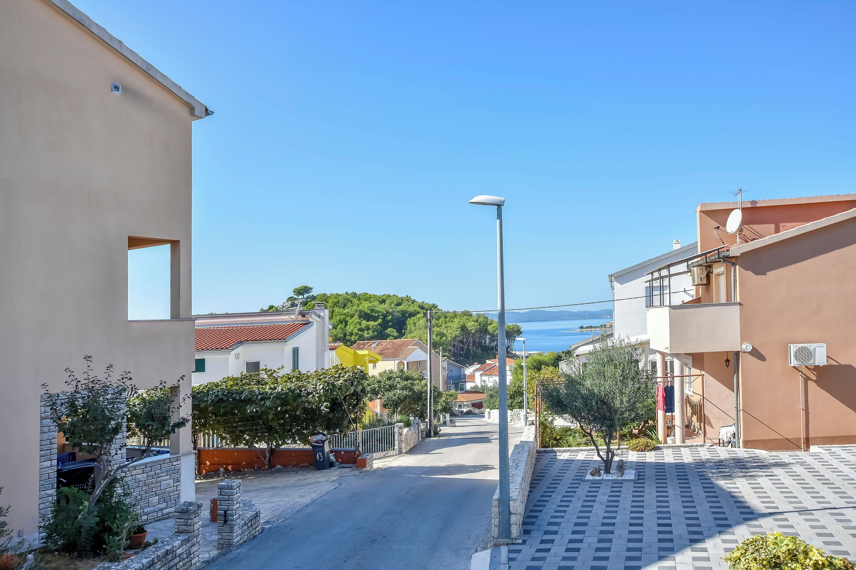Una calle estrecha flanqueada por edificios, cielo despejado y una vista distante del mar.