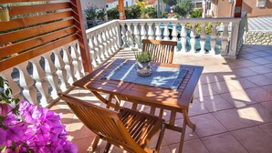 A wooden table with chairs on a balcony with a white balustrade, a potted plant, and purple flowers. - Apartment Burin (Pakostane)
