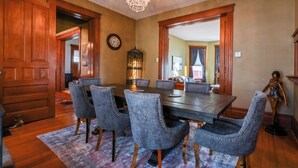 A dining room with a large wooden table, six upholstered chairs, a chandelier, and a birdcage. - Bricks & Chance Luxury 5 BR home, NEAR Benedictine (Atchison)