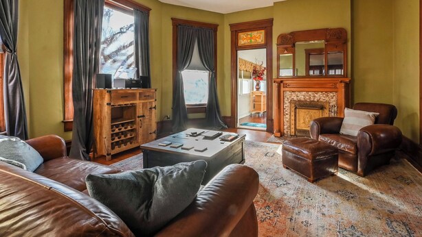 A cozy living room with a fireplace, leather furniture, and a large window with curtains. - Bricks & Chance Luxury 5 BR home, NEAR Benedictine (Atchison)