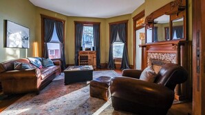 A living room with a brown leather sofa, a wooden coffee table, and a fireplace. - Bricks & Chance Luxury 5 BR home, NEAR Benedictine (Atchison)