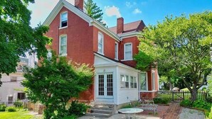 A two-story brick house with a small attached garage, a front porch, and a well-maintained garden with a brick pathway. - Bricks & Chance Luxury 5 BR home, NEAR Benedictine (Atchison)