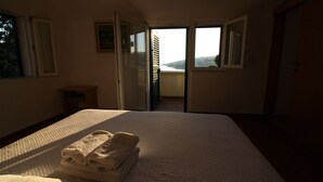 Ein Hotelzimmer mit einem großen Bett, Blick durch eine offene Tür und einem kleinen Tisch mit einer Lampe.