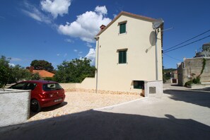 A two-story building with a tiled roof, a satellite dish, and a parked red car. - Apartment and Room Lada (Selca)