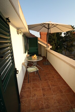 A small outdoor patio with a round table, two chairs, and a large umbrella. - Apartment and Room Lada (Selca)