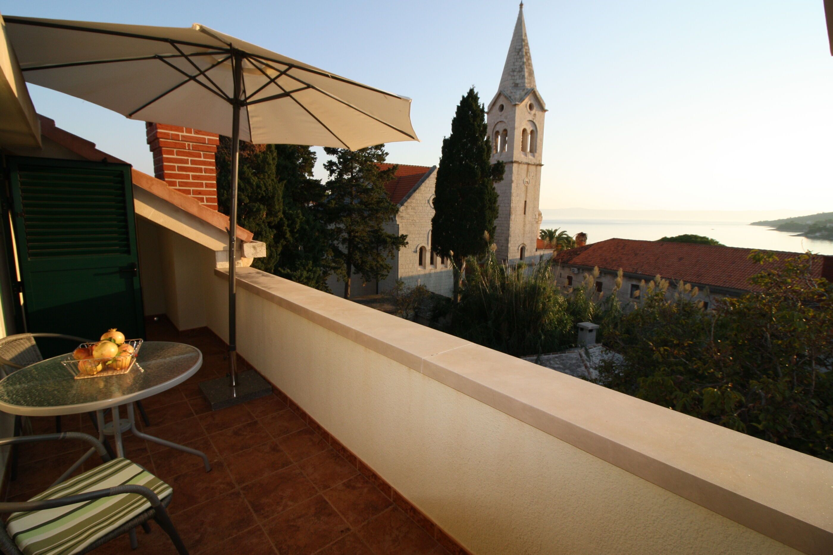 Un balcón con mesa y sillas, un gran parasol y vistas a una iglesia y la costa.