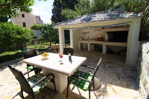 En udendørs terrasse med et bord og stole, et grillområde og en stenbelagt gulv.