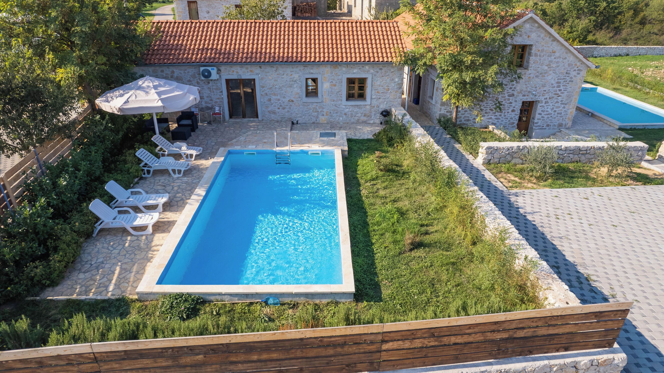 A stone house with a swimming pool, surrounded by greenery and a wooden deck.