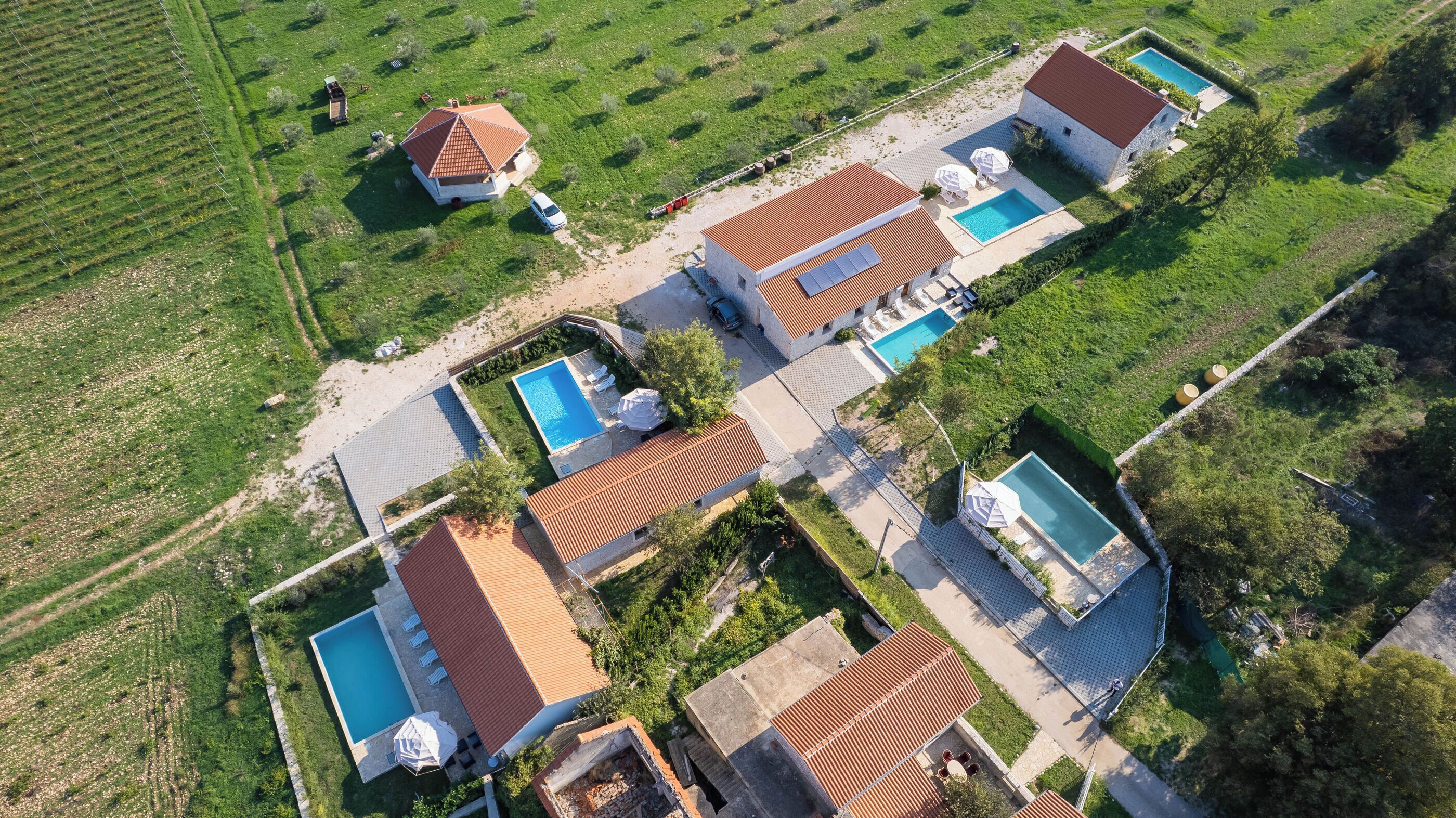 An aerial view of a residential area with multiple houses, each featuring a swimming pool and a garden.