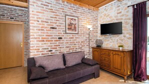 A cozy living room with a brick wall, a wooden ceiling, a brown sofa, a wooden cabinet, and a flat-screen TV. - House Stone Curlew 2 (Benkovac)