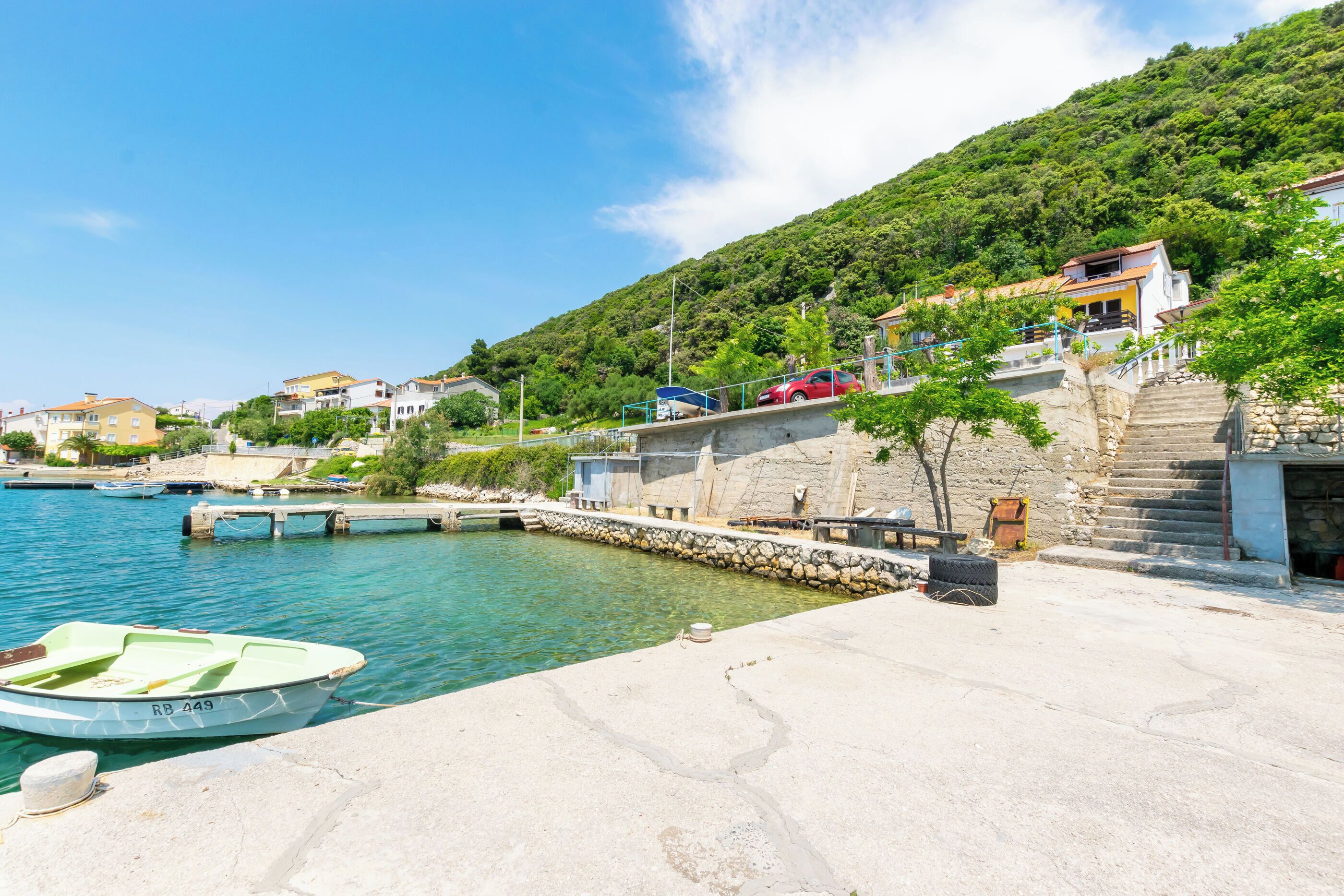 Una località costiera con un porto turistico, scale in pietra che conducono alle case e una piccola barca ormeggiata al molo.