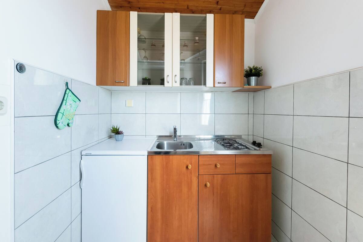 A compact kitchen with white cabinets, a stainless steel sink, and a wooden countertop.