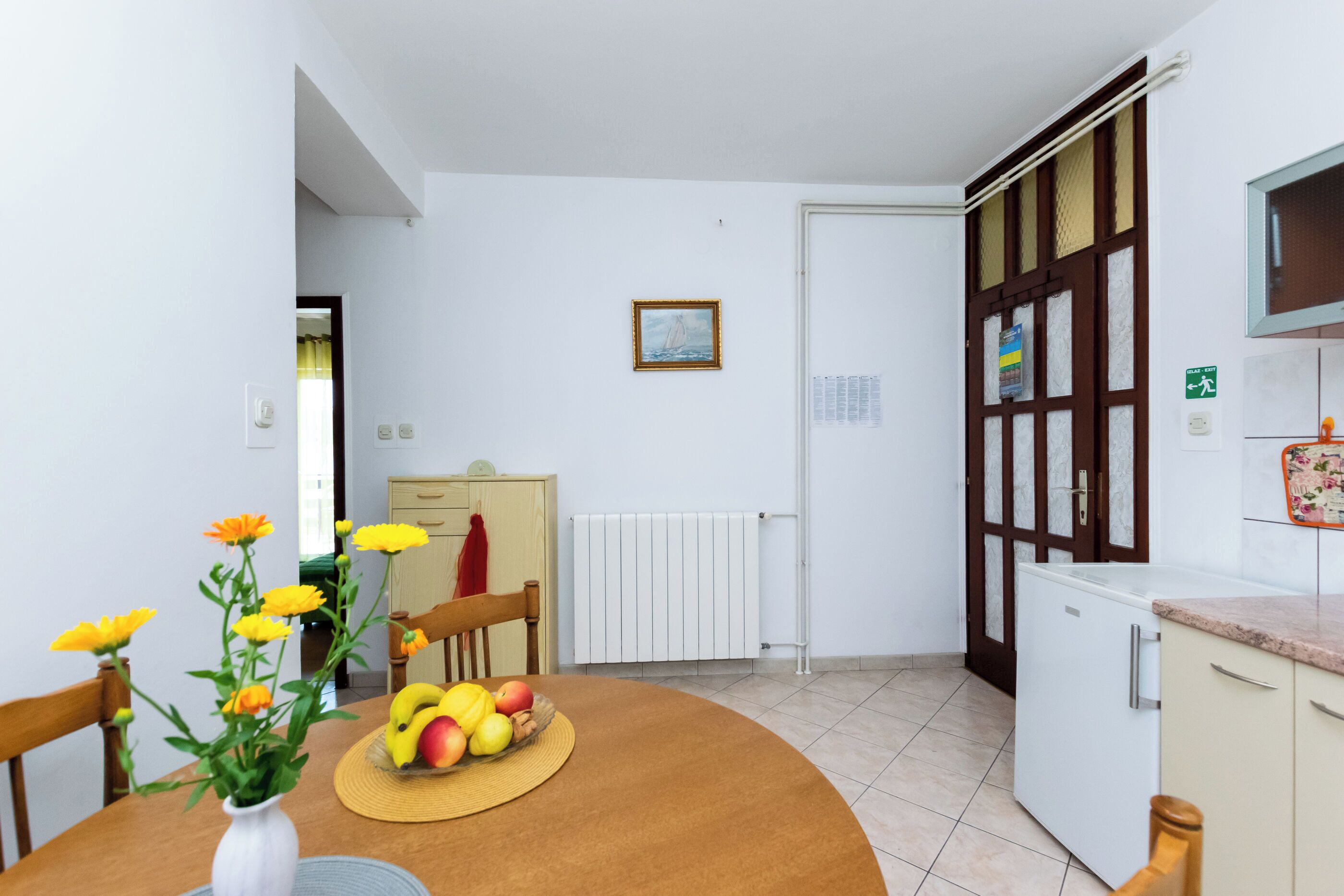 A kitchen with a dining table, a fruit bowl, and a vase of flowers.