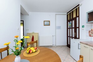 A kitchen with a dining table, a fruit bowl, and a vase of flowers. - Apartments Luci (Rab)