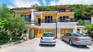 A two-story house with a yellow facade, a balcony, and a parked car in the driveway. - Apartments Luci (Rab)