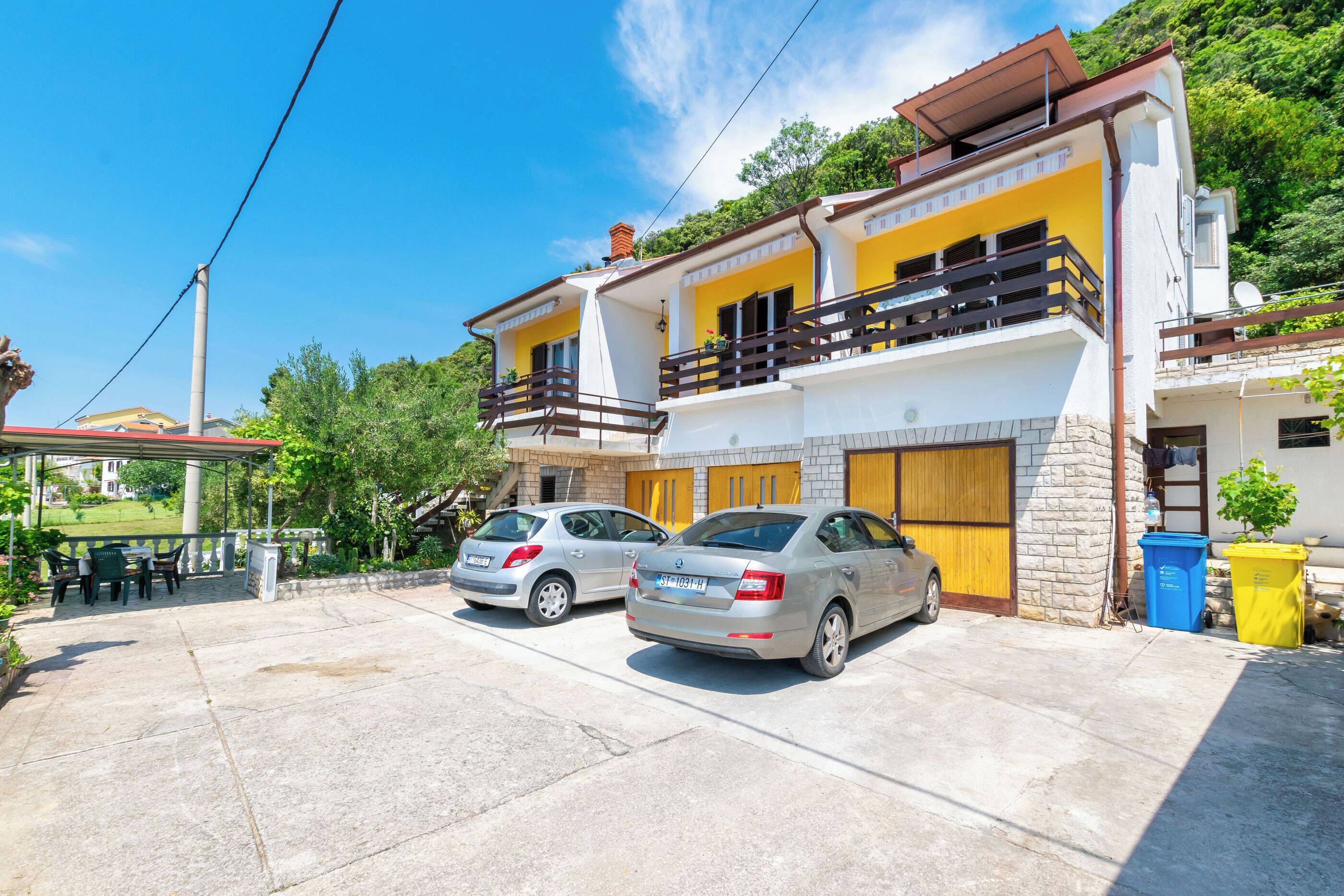 A two-story house with a balcony, parked cars, and a patio area.