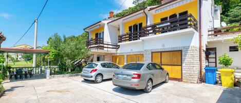 A two-story house with a balcony, parked cars, and a patio area.