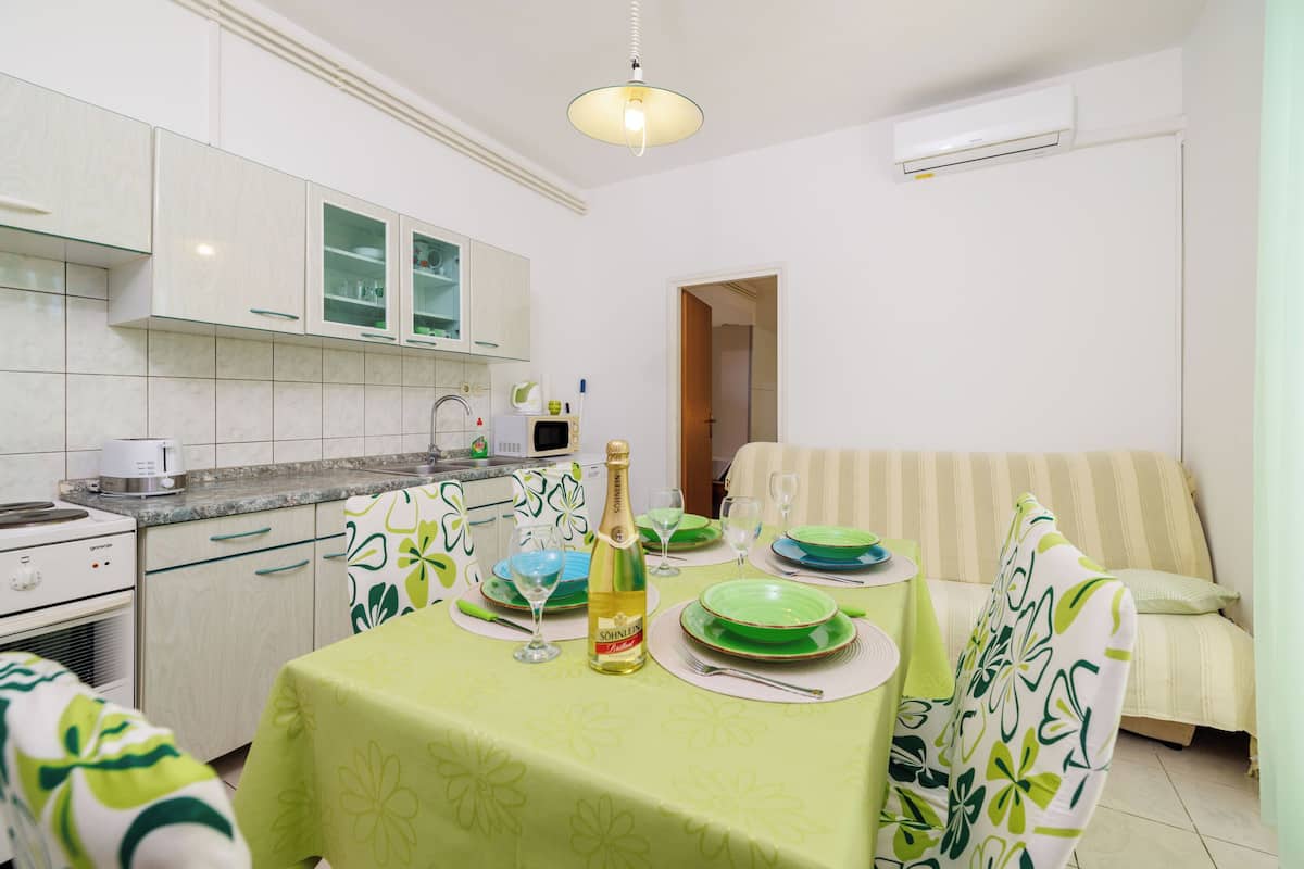 A dining area with a table set for two, a bottle of wine, and a sofa in the background.