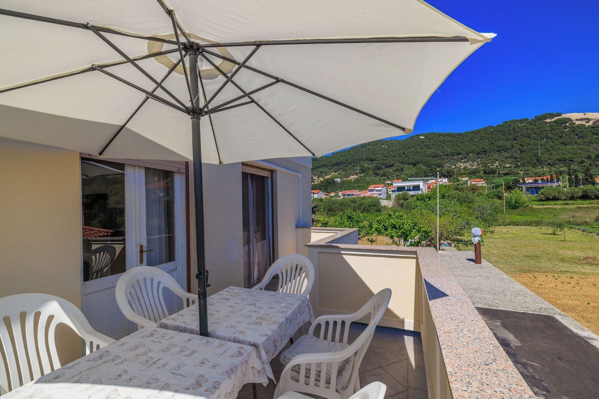 An outdoor patio with a table and chairs under a large umbrella, overlooking a hillside with buildings.