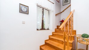 A wooden staircase with a handrail, a small table with a plant, and a window with curtains. - House Oleander (Sukosan)