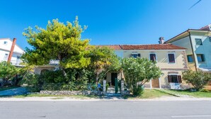 A two-story building with a tiled roof, a green door, and a stone wall in front. - House Oleander (Sukosan)