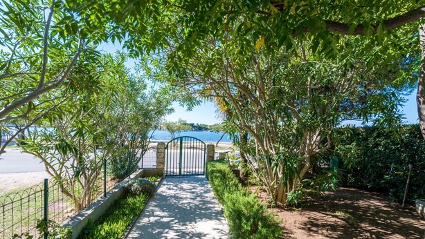 A pathway leading to a gated entrance with a view of a body of water. - House Oleander (Sukosan)