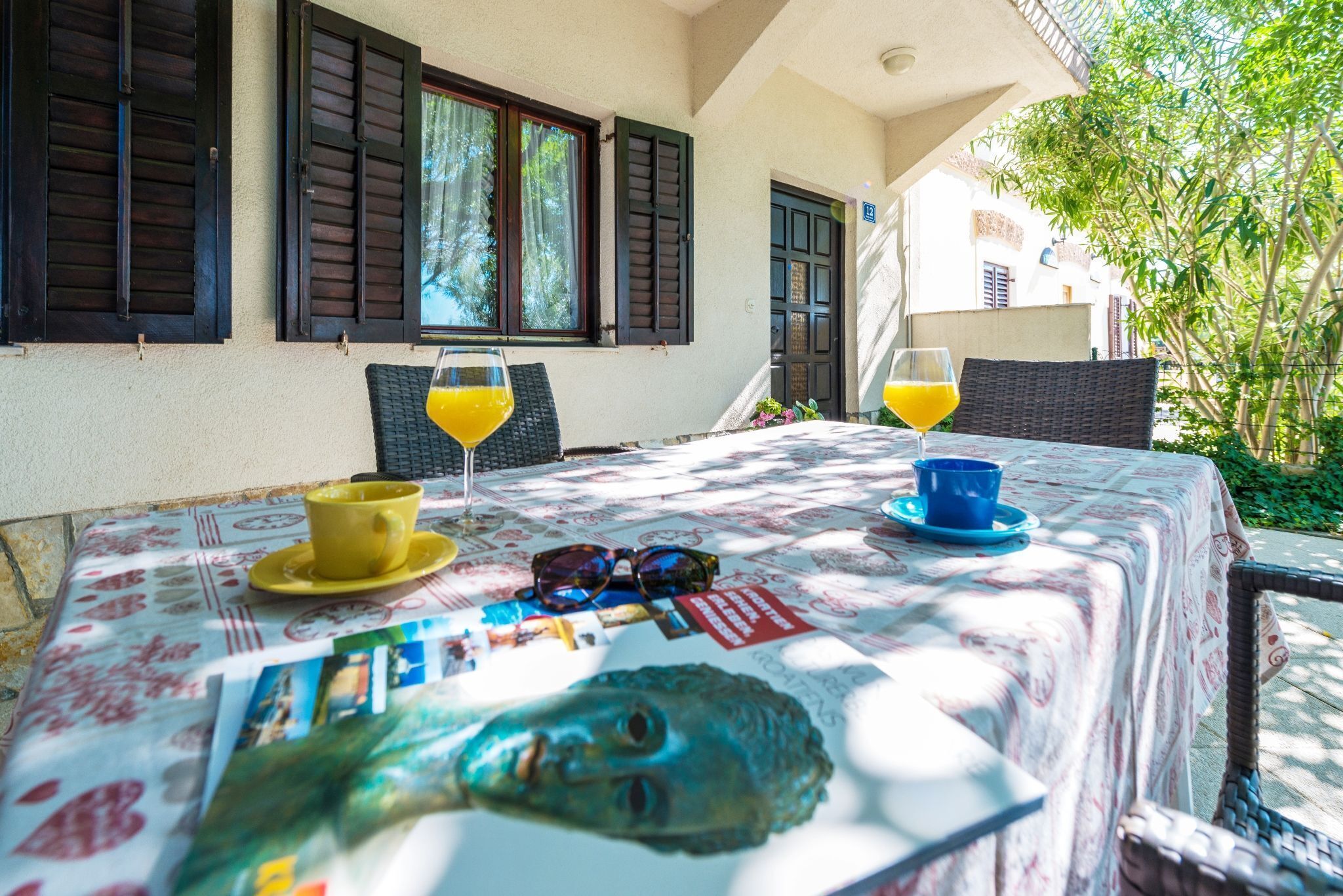 A table set with a yellow cup, a blue cup, and a glass of orange juice, with a magazine and sunglasses on it.