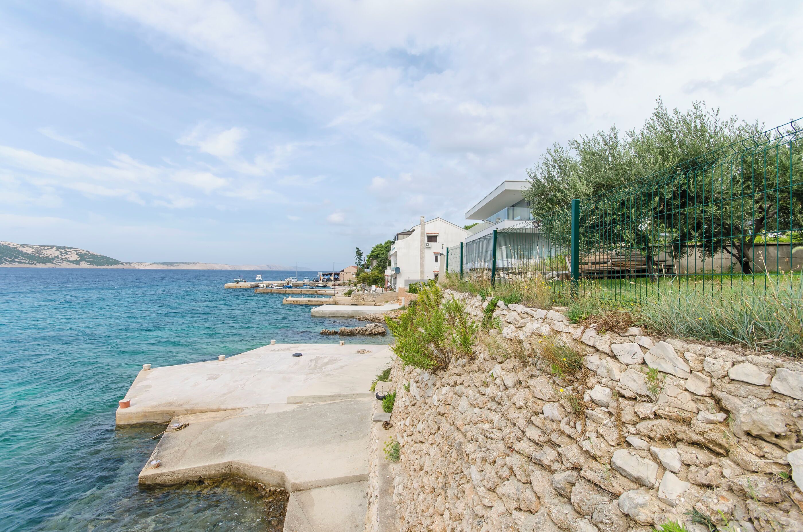 Una propiedad costera con un muro de piedra y un camino de hormigón que lleva a una casa frente al mar.
